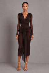 A woman modeling a dark brown long-sleeve bodysuit with a wrap-style V-neck bodice, worn with a mesh skirt with a tie thats gathered at waist, and sheer draped overlay, photographed against a plain grey studio background.