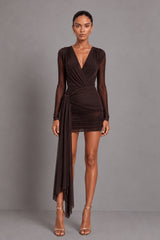 A woman modeling a dark brown long-sleeve bodysuit with a wrap-style V-neck bodice, worn with a mesh skirt with a tie thats gathered at waist, and sheer draped overlay, photographed against a plain grey studio background.