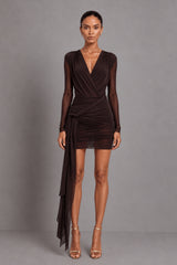 A model wearing a dark brown long-sleeve wrap bodysuit with sheer mesh sleeves and a draped side detail skirt, paired with metallic high-heeled sandals, against a solid gray studio background.
