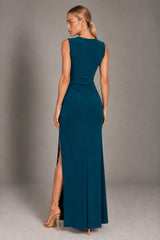 A woman modeling a sleeveless floor-length teal gown from the back, standing against a plain gray studio backdrop.