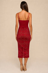A woman viewed from the back wearing a fitted red spaghetti-strap dress with a lace skirt, paired with beige high-heeled sandals, against a plain beige studio background.