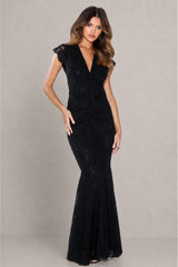 A woman modeling a black lace mermaid gown with cap sleeves and a deep V-neckline, standing against a neutral gray studio backdrop.