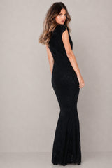 A woman modeling a sleeveless black mermaid gown with a high neck and sheer textured overlay, photographed against a neutral light gray studio background.
