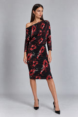 A woman models a black off-the-shoulder midi dress with a red and white floral pattern, paired with black high heels, against a neutral gray studio background.