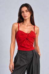 A woman modeling a bright red spaghetti-strap top with a large gathered sweetheart neckline and front twist detail, paired with dark charcoal gray wide-leg trousers, against a solid light gray studio background.