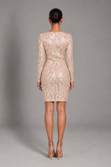 A woman viewed from the back wearing a fitted long-sleeve lace mini dress in a light warm beige tone, paired with nude high-heeled sandals, against a plain gray studio background.