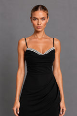 A woman modeling a black spaghetti-strap dress with a sweetheart neckline and a silver rhinestone embellished trim, set against a solid gray studio background.
