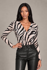 A woman modeling a beige and black zebra-print long-sleeve wrap top paired with black faux-leather pants, against a solid gray studio background.
