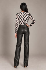 A woman shown from the back wearing a beige and black zebra-print long-sleeve top and black faux-leather pants, standing against a neutral gray studio background.