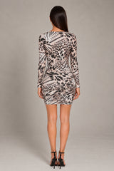 A woman viewed from the back wearing a fitted long-sleeve mini dress with an abstract animal-inspired print in beige, black, and gray, paired with black high-heeled sandals against a plain light gray studio background.