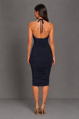 A woman modeling the back of a sleeveless, halter-neck midi dress in dark navy blue. The dress features a ruched bodice and a fitted, ruched skirt.