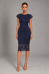 A woman modeling a navy blue lace knee-length dress with cap sleeves and sheer lace heels, standing against a neutral gray studio background.