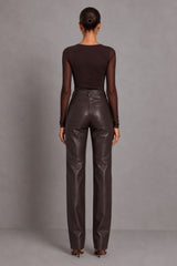A model viewed from the back wearing a dark brown sheer long-sleeve top and matching dark brown faux-leather straight-leg pants, set against a plain gray studio background.