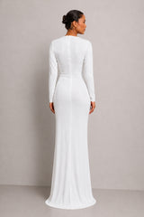 A woman viewed from the back wearing a fitted long-sleeve white maxi dress with a structured waist seam, standing against a plain light gray studio background.