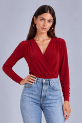 A woman modeling a long-sleeve red wrap-style top with a deep V-neck and gathered neckline, paired with light blue jeans, against a plain light gray studio background.