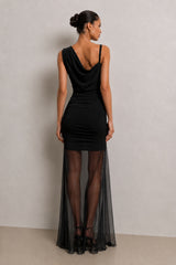 A woman modeling a black one-shoulder cowl-neck dress with long sheer skirt, shown from the back against a neutral studio backdrop.