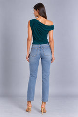 A woman shown from the back wearing a dark teal off-the-shoulder draped top, light blue straight-leg jeans, and tan high-heeled sandals against a light gray studio background.