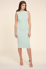 Model wearing a mint green sleeveless midi dress photographed from the front. The fitted dress features a high round neckline, a smooth, minimalist silhouette with subtle shaping through the waist and hips, and a knee-length hem. The model wears nude strappy high-heeled sandals and has long, straight brown hair styled with a centre part. She is standing against a soft warm beige studio background.