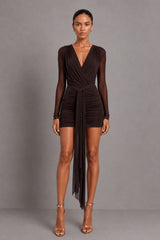 A woman modeling a dark brown long-sleeve bodysuit with a wrap-style V-neck bodice, worn with a mesh skirt with a tie thats knotted  at the front, and sheer draped overlay, photographed against a plain grey studio background.