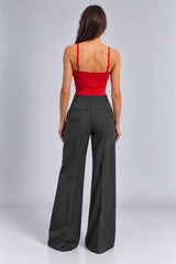 A woman shown from the back wearing high-waisted, wide-leg charcoal gray pants and a bright red spaghetti-strap crop top, photographed against a light gray studio background.