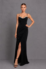 A woman modeling a floor-length black evening gown with thin straps, a sweetheart neckline, and a high front slit, photographed against a plain gray studio background.