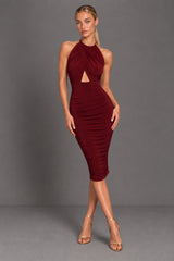 A woman modeling a sleeveless, halter-neck midi dress in dark berry. The dress features a ruched bodice with a keyhole cutout at the waist and a fitted, ruched skirt.