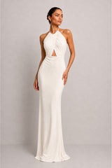 A woman modeling a floor-length halter gown in a warm off-white or cream shade against a plain light gray studio background.