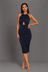 A woman modeling a sleeveless, halter-neck midi dress in dark navy blue. The dress features a ruched bodice with a keyhole cutout at the waist and a fitted, ruched skirt.