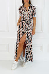 A model wearing a long sleeved maxi shirt dress with a geometric pattern in black and white colors. The dress features a V-neckline, a waist tie belt, and pockets.