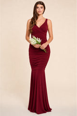 Woman wearing a burgundy berry evening bridesmaids maxi dress gown holding flowers against a beige background