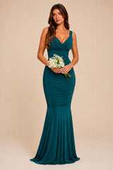 Woman in a teal green evening maxi bridesmaid gown holding flowers against a beige background 