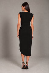 A woman viewed from the back wearing a sleeveless black midi dress with a defined waist seam, paired with black strappy high heels, against a neutral gray studio backdrop.