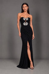 A woman modeling a strapless black evening gown with a sweetheart neckline, sheer mesh keyhole detail at the bust, and a high front slit, photographed against a plain gray studio backdrop.