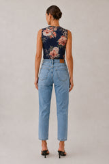 A woman shown from the back wearing a sleeveless navy floral top and light-wash blue cropped jeans, standing against a plain light gray studio background.