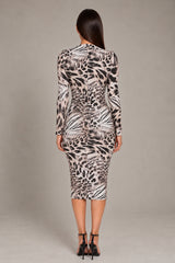A woman viewed from the back wearing a fitted long-sleeve midi dress with an animal-print pattern in black, white, and beige, paired with black high-heeled sandals against a plain light gray studio background.