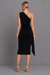 A woman modeling a black one-shoulder midi dress from the back, paired with metallic gold high heels, set against a solid gray studio background.