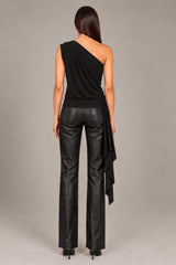 A woman shown from the back wearing a black one-shoulder wrap top and black faux-leather wide-leg pants, standing against a neutral gray studio background.