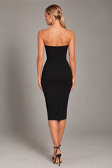 A woman modeling a strapless black midi dress from the back, standing against a neutral gray studio background.