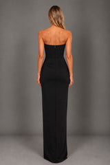 A woman viewed from the back wearing a strapless black floor-length gown against a plain gray studio backdrop.