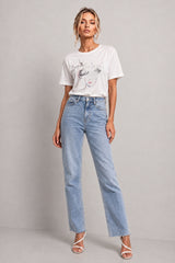 A woman modeling a white graphic t-shirt and light-wash blue straight-leg jeans against a neutral gray studio background.