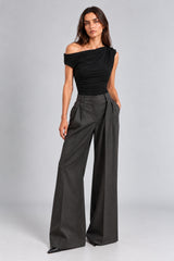 A model wearing a black off-the-shoulder ruched top and dark charcoal gray wide-leg trousers, standing against a light gray studio background.