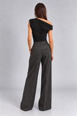 A woman shown from the back wearing a black off-the-shoulder top and dark charcoal wide-leg trousers, standing against a light gray studio background.