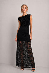 A woman modeling a black one-shoulder lace maxi dress with a velvet-like upper bodice and a sheer floral lace lower skirt, standing against a plain light gray studio background.