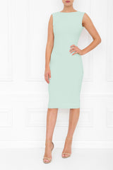 Model wearing a mint green sleeveless midi dress photographed from the front. The fitted dress features a high round neckline, a smooth, minimalist silhouette with subtle shaping through the waist and hips, and a knee-length hem. The model wears nude strappy high-heeled sandals. She is standing against a white  studio background.